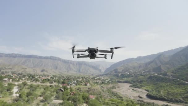 Quadcopter κρέμεται στον αέρα πάνω από την πράσινη κοιλάδα και την καλλιέργεια δέντρων. Πάμε. Drone με περιστρεφόμενες λεπίδες πάνω από βουνά σε θολό φόντο του ουρανού. — Αρχείο Βίντεο