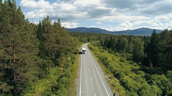 Top view of truck driving along highway in forest area. Scene. Truck is driving along highway among green forest on background of mountains. Truck goes along route in forest area on sunny summer day — 图库照片
