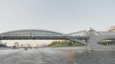 Nehirde cam köprüsü olan yüzen bir teknenin görüntüsü. Başla. Şehrin arka planında ve cam köprüde güzel bir nehir manzarası. Açık güneşli bir günde modern jöleli köprü