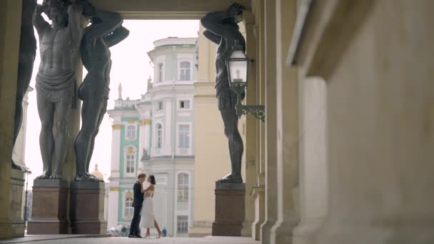Beautiful newlyweds hug at old building. Action. Small silhouette of newlyweds in distance under arch of tall statues. Beautiful shot with tall statues under arch of building and newlyweds — Video Stock