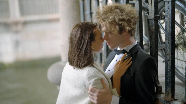 Mariée passionnée et marié embrassant par la porte de fer. L'action. Sexy jeune homme et femme en costume et robe blanche par temps venteux. — Photo
