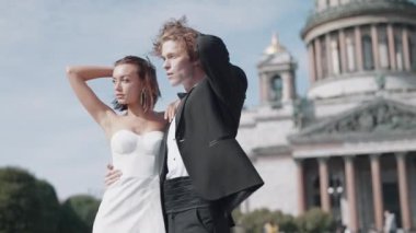 Eski mimarinin arka planında güzel yeni evliler. Başla. Güneşli bir günde katedralin arka planında poz veren zarif bir çift. Yeni evliler yazın rüzgarlı ve güneşli bir günde