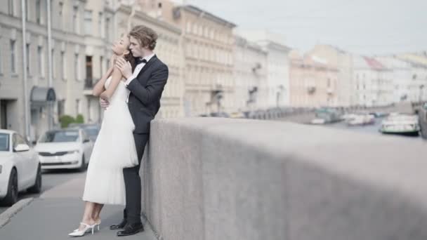 Hermosa pareja de recién casados abrazando en el fondo de la ciudad. Acción. Sesión de fotos para recién casados en un entorno urbano. Hermosos recién casados abrazan en la ciudad con la vieja arquitectura — Vídeos de Stock