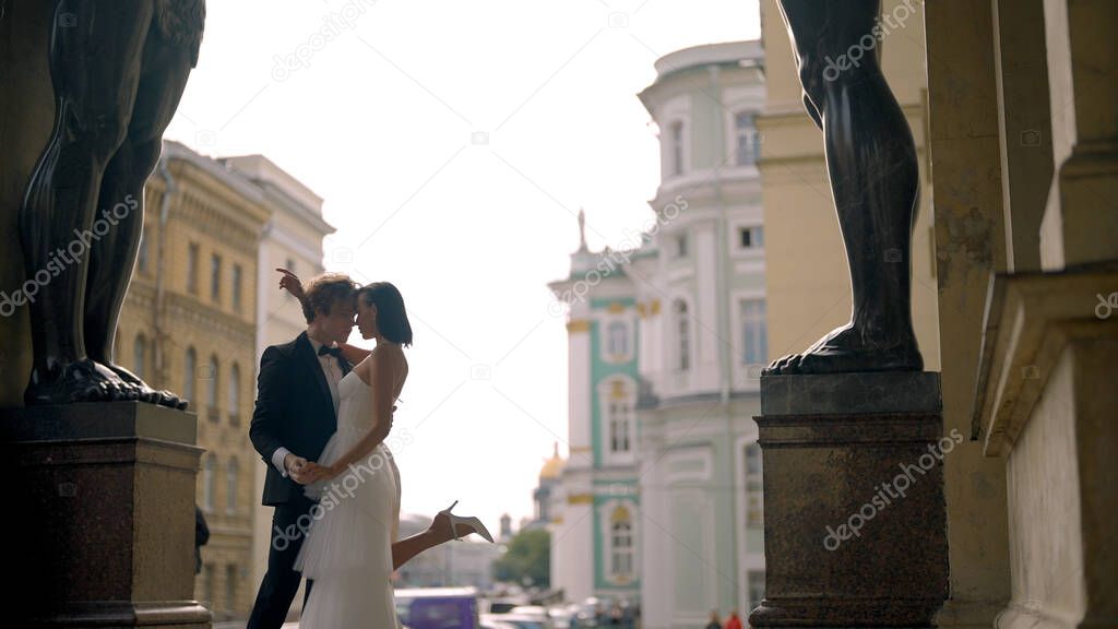 Photosession of a beautiful elegant wedding couple inside the porch of the New Hermitage by the feet of atlantes. Action. Loving Bride and groom embracing at the historical center of Saint Peterburg