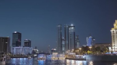 Parlayan modern şehirli gemileri olan şehir nehri. Başla. Modern şehrin güzel gökdelenleri gece nehir kenarında parlıyor. Geceleri şehir manzarası olan nehirde yüzen gemiler.