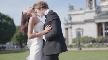 Güzel yeni evliler. Başla. Bir çift aşık, dar beyaz elbiseli gelin ve uzun saçlı damat sokakta setin ve güzel tarihi binaların yanında poz veriyor.