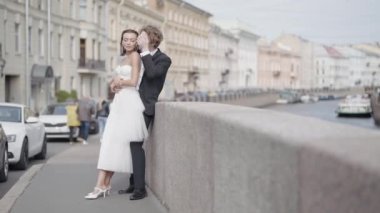 Güzel yeni evliler. Başla. Bir çift aşık, dar beyaz elbiseli gelin ve uzun saçlı damat sokakta setin ve güzel tarihi binaların yanında poz veriyor.