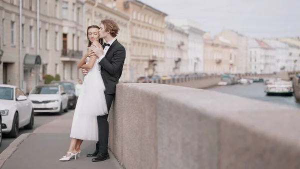 Seitenansicht des fürsorglichen schönen frisch verheirateten Paares, das sich am Granitbürgersteig umarmt. Handeln. Elegantes Brautpaar draußen auf der Straße. — Stockfoto