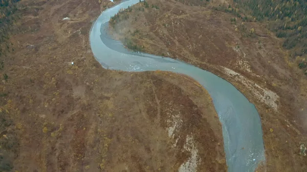 De natuur vanaf de hoogte van een drone. Een knip. De blauwe heldere kronkelende rivier naast het grijze bos stroomt door de bergketens. — Stockfoto