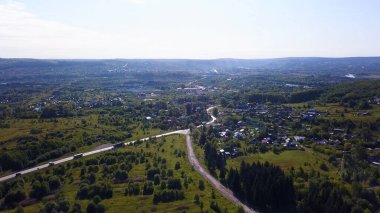 Helikopterden yaz manzarası. Şarjör. Otoyolu olan küçük bir kasaba, konut binaları, konut binaları, parklar ve ormanlar ve etrafındaki ağaçlar güneşli gökyüzünde.