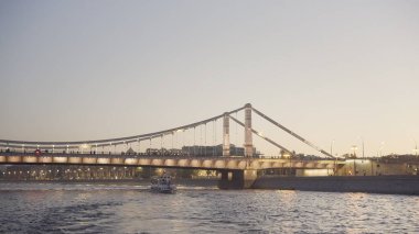 Nehir parlayan köprüsü ve yüzen teknesi olan güzel şehir manzarası. Başla. Gün batımında parlayan köprünün arka planında tekne nehirde yüzer.