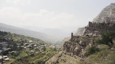 Dağ yamacında terk edilmiş taş duvarları olan antik köyün kalıntıları. Başla. Yaz uçurumu ve bulutlu arka planda kayanın yanındaki yerleşim yeri.