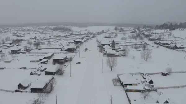 Snowy birds-eye view. Clip. A white village in the snow with small wooden houses and next to it a large forest with tall trees — Stock Photo, Image