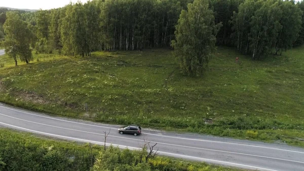 Vista aérea de uma paisagem rural com a estrada e floresta verde. Cena. Um carro de passageiros dirigindo na estrada através de colinas verdes rolando cênica com árvores e vegetação. — Fotografia de Stock