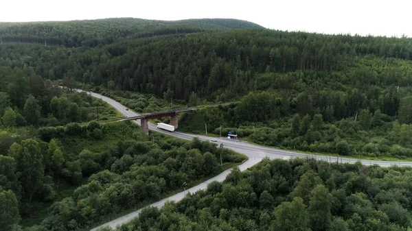 Вид с воздуха на сельскую местность с шоссе и зеленым лесом. Сцена. Грузовик и пассажирский автомобиль едут по шоссе через живописные зеленые холмы с деревьями и растительностью. — стоковое фото