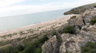 Kayaların ve deniz kıyısının havadan görünüşü, yaz ve tatil konsepti. Başla. Yeşil çalılarla taşın ve kumsalın üzerinde uçuyor..