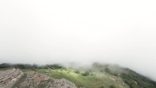 霧の中で驚くほど珍しい岩や緑の芝生の上を飛ぶ。行動だ。山頂と雲の空中風景. — ストック動画