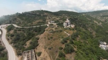 İnsansız hava aracının görüntüsü. Başla. Denizin yanındaki güzel yeşil dağların manzarası. Üzerinde bir tapınak, yüksek ağaçlar, yollar ve bir plaj var.