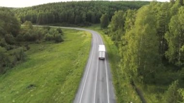 Kuş bakışı manzaralı güzel bir yaz manzarası. Sahne. Sürücü arabalarla dolu uzun bir yol ve arkasında uzun ağaçlar olan kocaman yeşil bir orman ve arkasında küçük evleri olan mavi berrak bir köy.