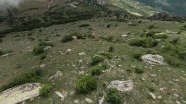 Dağ yamaçlarında uçan bir dron. Başla. Yeşil yamaçların üzerinde taşlı güzel bir uçuş. Yazın tepelerin ve dağların zirvesinin manzarası
