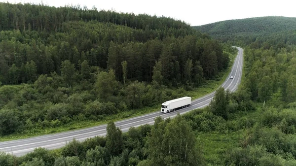Vue aérienne d'un drone d'une voiture de camion conduisant sur une route courbée parmi les arbres verts. Scène. Voiture longue cargaison blanche sur la route vide près de la forêt d'été. — Photo