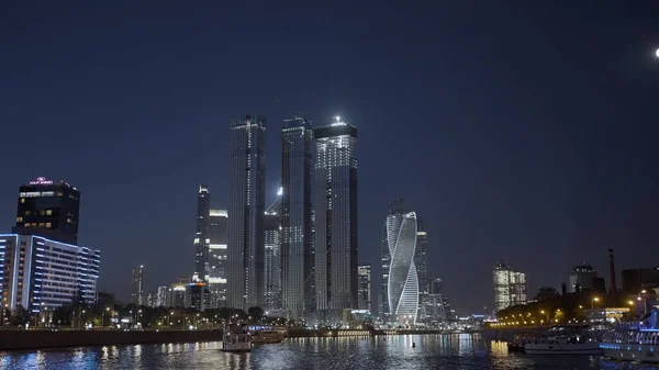 Goedenavond stad. Actie. Enorme hoge avondgebouwen gelegen aan de rivier en alles is verlicht met lantaarns. — Stockfoto