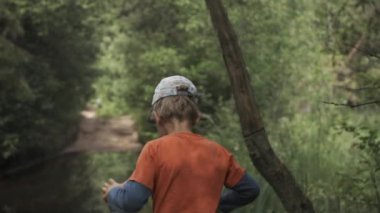 Küçük bir oğlan. Yaratıcı. Parlak yaz kıyafetleri içinde bir çocuk güzel küçük bir gölün yanında ormanda yürüyor..