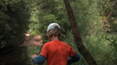 Küçük bir oğlan. Yaratıcı. Parlak yaz kıyafetleri içinde bir çocuk güzel küçük bir gölün yanında ormanda yürüyor..