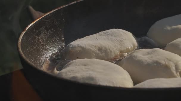 Piték egy serpenyőben. Kreatív. A tésztát forró serpenyőben sütik. Forr az olaj. Ételsütés a természetben nyílt tűzön — Stock videók