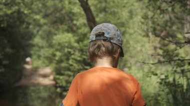 Çocuk yaz ormanlarında yürüyor. Yaratıcı. Çocuk güneşli bir günde orman yolunda tek başına yürüyor. Yaz ormanlarında yürüyorum.