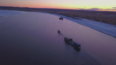 Kargo nakliye gemisi yaz şafağında geniş bir nehirde yelken açıyor. Şarjör. Gün batımına doğru sonsuz alan boyunca yüzen mavnanın hava manzarası, su taşımacılığı kavramı..