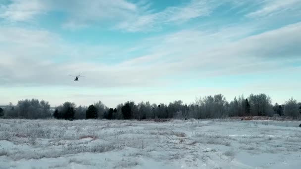 Ελικόπτερο προσγείωση σε ένα χιονισμένο πεδίο με το δάσος και συννεφιασμένο ουρανό στο παρασκήνιο. Κλιπ. Ανεβαίνει μεγάλη χιονοθύελλα, ενώ προσγειώνεται σε ένα χειμερινό πεδίο. — Αρχείο Βίντεο