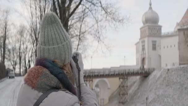 Une femme en vêtements chauds prenant des photos de la belle architecture de la vieille ville d'hiver sur un appareil photo. L'action. Concept de tourisme et de voyage. — Video