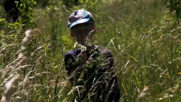 Портрет маленького бота, стоящего с закрытыми глазами в длинной траве. Творческий подход. Мальчик на летнем лугу с качающейся на ветру травой. — стоковое видео