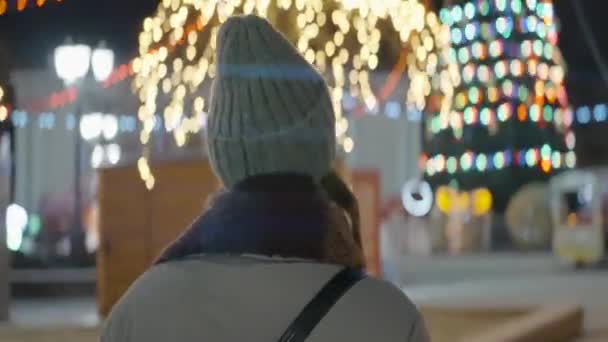 Mooie vrouw gaat 's nachts naar de kerstboom. Actie. Nachtwandeling door versierde kerststad. Vrouw loopt rond Nieuwjaar stad 's nachts in de winter — Stockvideo