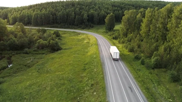 从鸟瞰的角度来看美丽的夏季风景。场景：一条长长的道路，开着汽车，还有一个巨大的美丽的绿树成荫的森林，后面是一个有小房子和蓝色的净光的村庄 — 图库照片