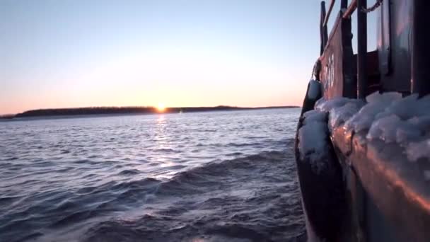 Vista desde el barco. Clip. Un barco con una pequeña cantidad de nieve flotando hacia adelante en el que las olas del río se rompen y desde lejos se puede ver el sol brillante saliente y el bosque. — Vídeo de stock