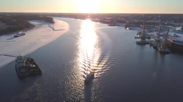 Vista desde un helicóptero. Clip. Un paisaje primaveral donde grandes barcos exportan carga a lo largo del río junto a bosques desnudos ligeramente nevados. — Vídeo de stock