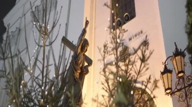 Etrafında yanan çelenkler olan küçük, güzel bir anıt. Başla. Köknar ağacından dalları olan beyaz bir bina yanında parlayan fenerler var ve her şey Noel 'le süslenmiş.