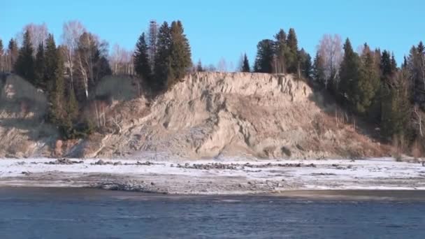 Přírodní krajina s řekou na začátku zimy a kopcovité pobřeží pokryté stromy. Klip. Kamenný útes s lesem a studenou řekou. — Stock video