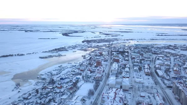 Winterblick aus einer Drohne. Ein Blick auf die Stadt aus einer Höhe, in der alle Häuser mit Schnee bedeckt sind, man sieht Straßen mit Autos, einen zugefrorenen Fluss und ein paar Bäume und einen strahlenden Himmel ohne Wolken.. — Stockfoto