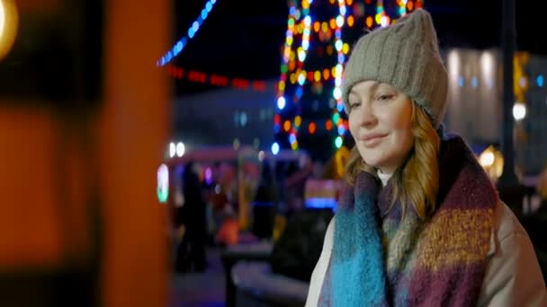 Kobieta na ulicy miejskiej z oświetleniem świątecznym. Akcja. Kobieta w ciepłych ubraniach patrzy na witrynę sklepu i uśmiecha się. — Wideo stockowe