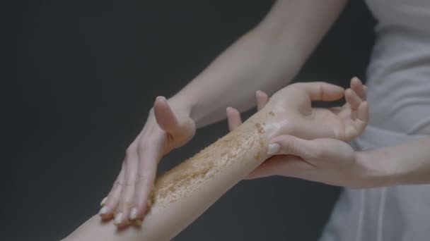 Aplicação de esfoliação de açúcar corporal no braço do cliente feminino, conceito de cuidados com o corpo. Acção. Close up de mão cosmetologist feminino durante o procedimento de beleza no salão. — Vídeo de Stock