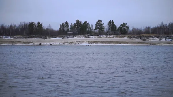 Noch nicht geschmolzener Schnee liegt auf der Landschaft am Flussufer. Der Fluss neben dem kahle Derwische und Schnee liegen — Stockfoto
