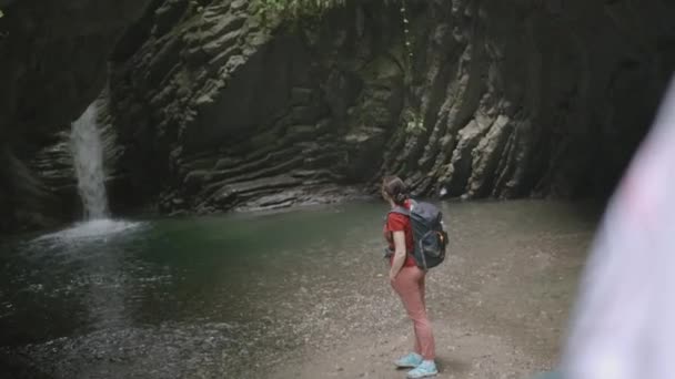 Het meisje kijkt naar de waterval. Dat is geweldig. Meisje kijkt naar de waterval in de bergen. Exotische plek met een waterval en een klein meer in de bergen — Stockvideo
