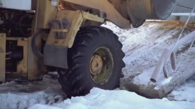 Buldozer kovayla bir şey çıkarıyor. Çıt. Sarı bir yürüyen merdivenin tekerlekleri ve kovasına yakın plan. Karda, bir buldozer ağır bir şey çektiğinde tekerleklerini çevirir.