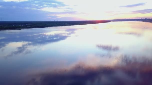 Kvadkoptern flyger på floden. Kom igen. Flodlandskap med en stad på andra sidan stranden mot bakgrund av solnedgången från fågelperspektiv — Stockvideo