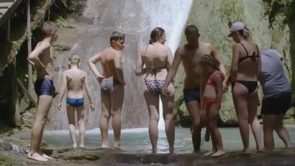 ГРИЦЕ, АФИНЫ - 27 апреля 2022 года: Восемь человек стоят у водопада КРИТИВ. Рядом с прудом находятся дети и взрослые. Веселая компания планирует плавать на фоне водопада — стоковое видео