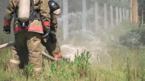 Feuerwehrleute. Clip. Zwei maskierte Männer, die mit einem Schlauch und Wasser Übungen mit speziellen Geräten und in einer speziellen Uniform durchführen. — Stockvideo