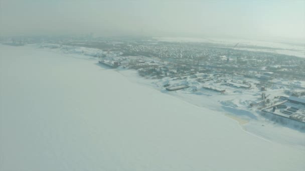 Зимний пейзаж с дрона.Клип.Белый пейзаж на замерзшем зимой городе, где дома и замерзшая река видны под большими сугробами. — стоковое видео
